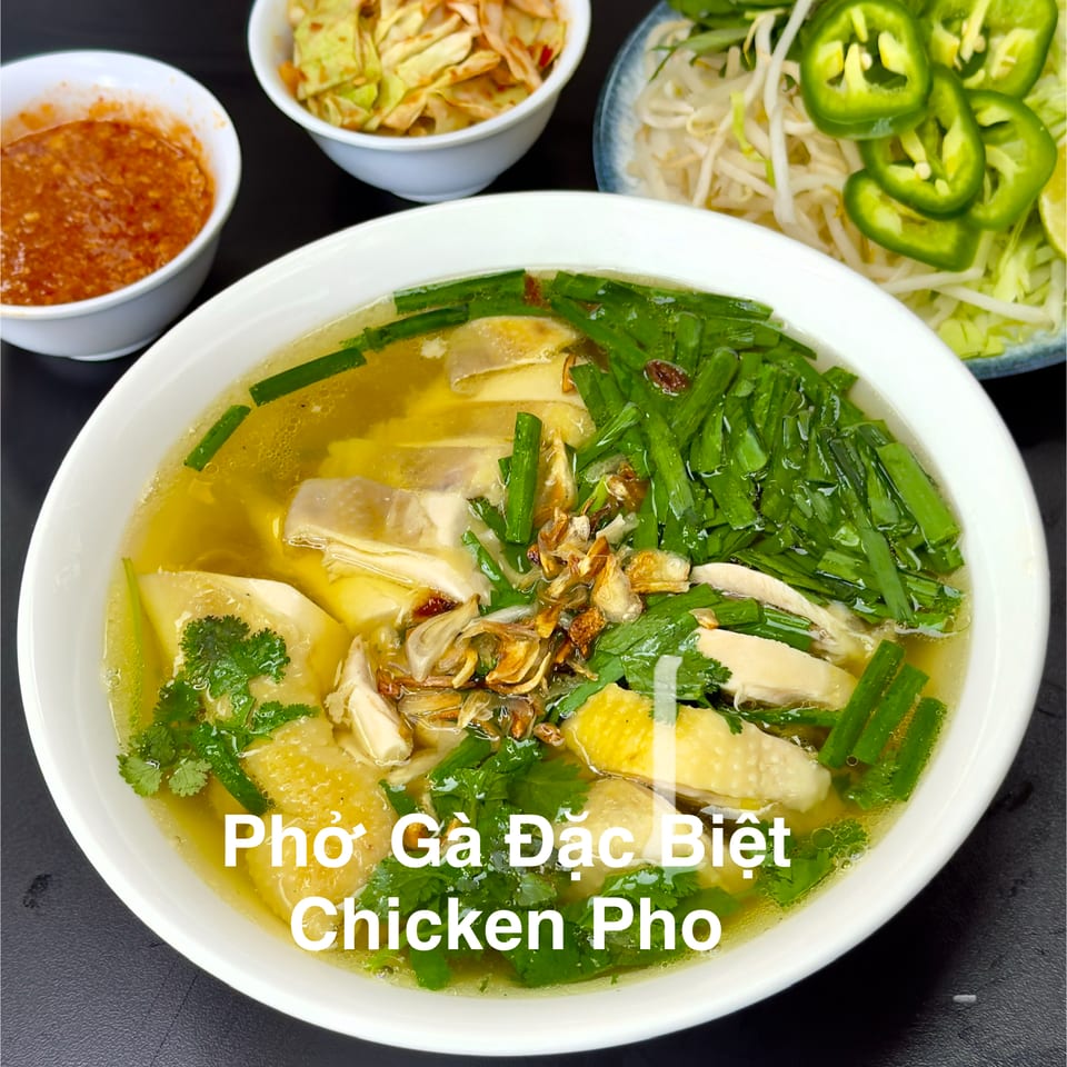 A bowl of chicken pho with broth, chicken, green onions, and cilantro, with side dishes.