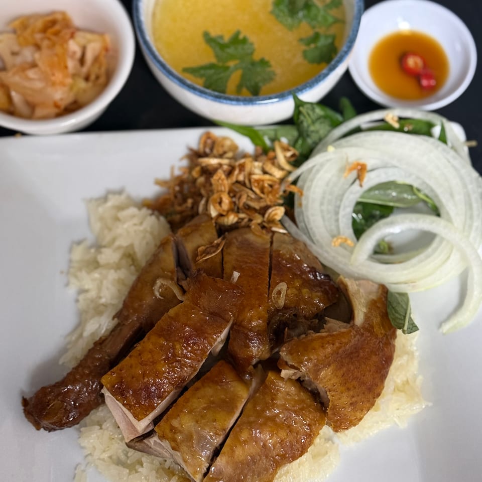 Platter of sliced roasted chicken with sticky rice, soup, kimchi, and chili sauce.