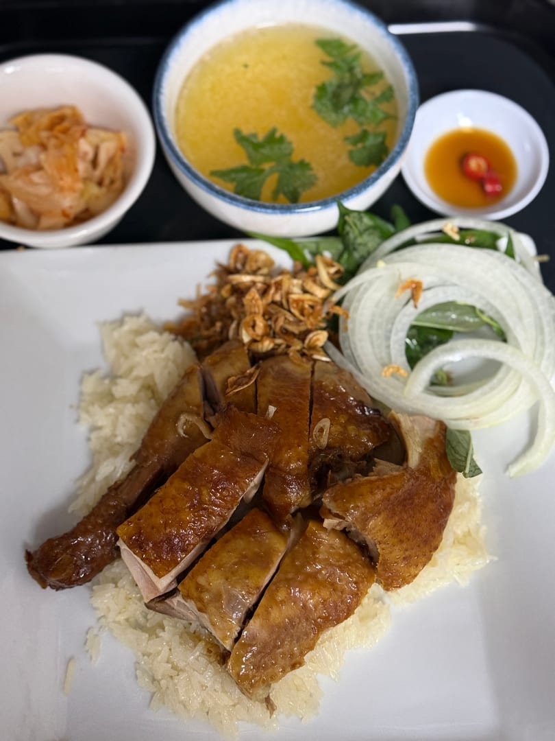 Platter of sliced roasted chicken with sticky rice, soup, kimchi, and chili sauce.