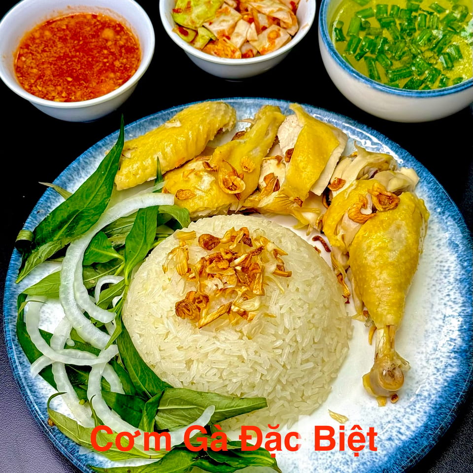 Com Ga Dac Biet, a Vietnamese chicken rice dish with sides of soup, chili sauce, and pickled cabbage.