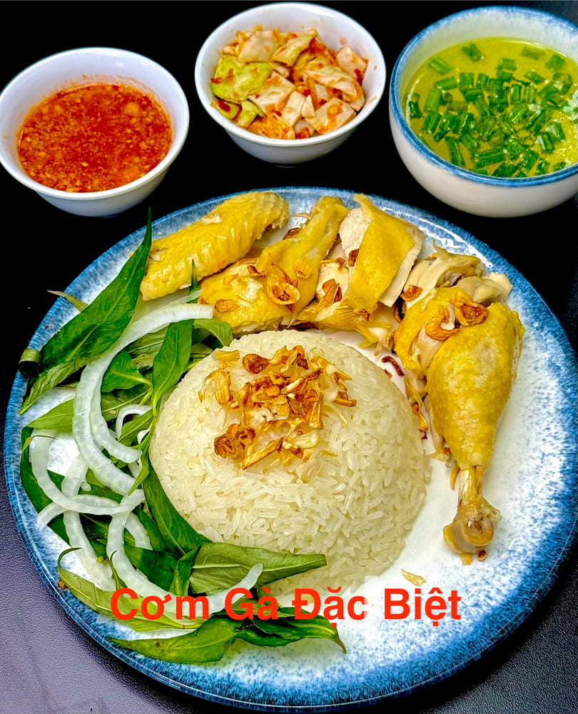 Com Ga Dac Biet, a Vietnamese chicken rice dish with sides of soup, chili sauce, and pickled cabbage.